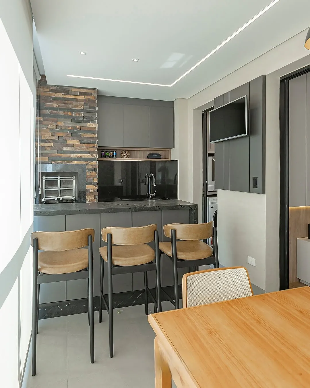 Área gourmet planejada em grafite com bancada e painel para televisão